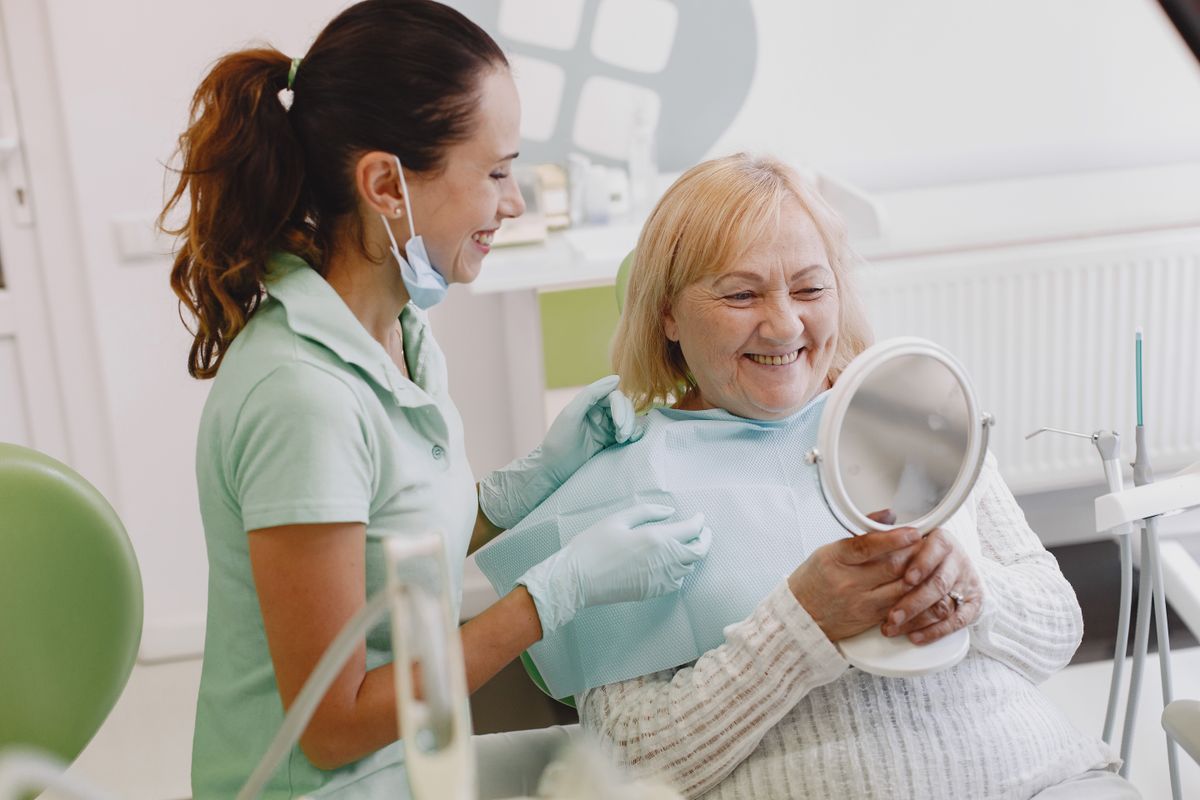 Paciente sorrindo ao se ver no espelho durante consulta odontológica (imagem ilustrativa)