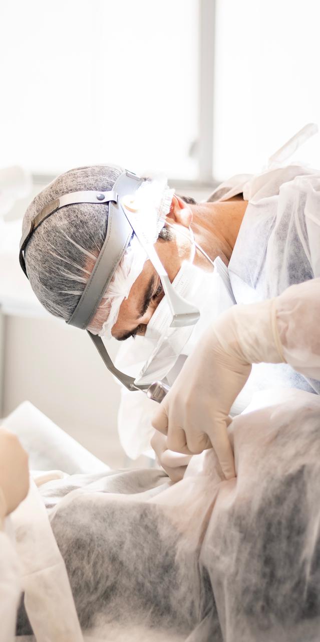 Dr. Michel Moraes concentrado durante um procedimento cirúrgico, com lupas e equipamento de proteção